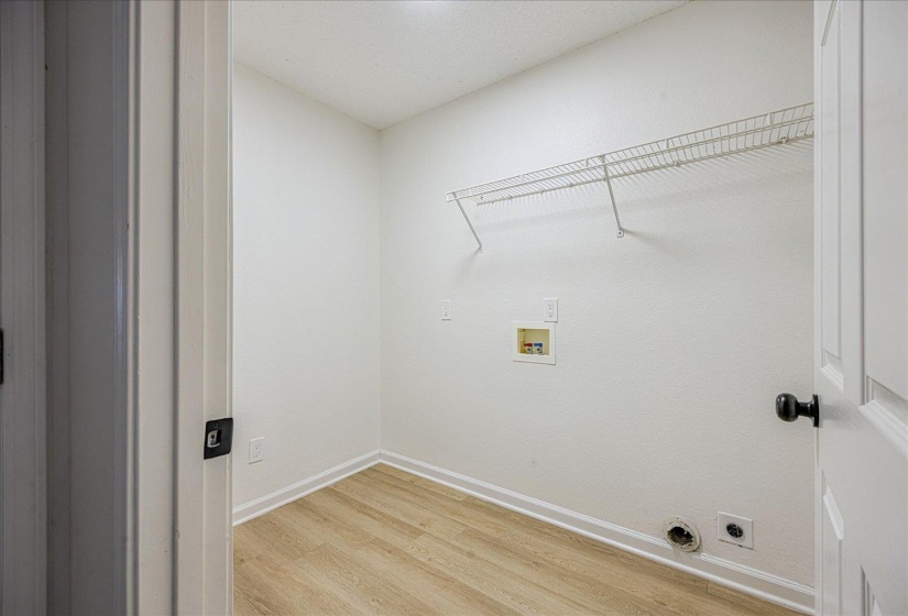 Laundry area featuring light wood-finish flooring, white walls, and a built-in wire shelf