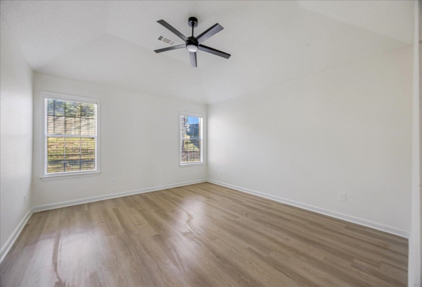 Spacious room featuring wood-finish flooring, white walls, and a vaulted ceiling with a modern black ceiling fan