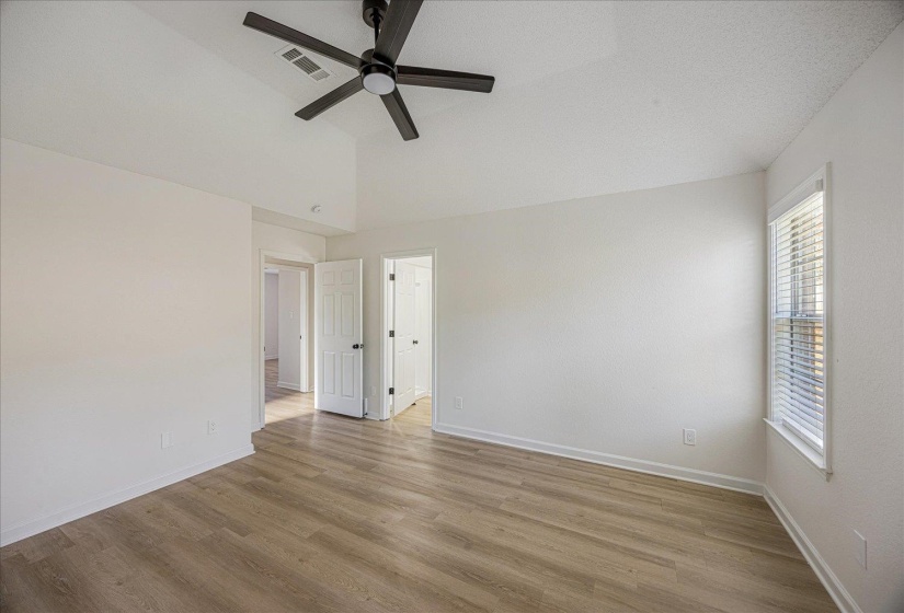 Spacious room featuring wood-finish flooring, vaulted ceiling, and a prominent window with blinds