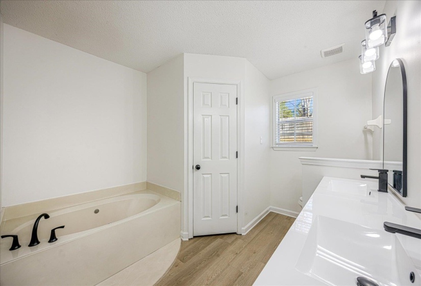White bathroom featuring a built-in soaking tub with dark-finish fixtures, a dual vanity with integrated sinks, and dark-finish faucets