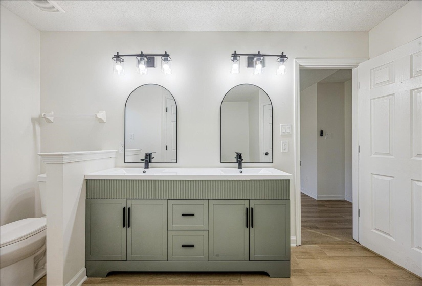 Dual sage green vanities with fluted detailing and matte black hardware, featuring integrated sinks and coordinating arched mirrors