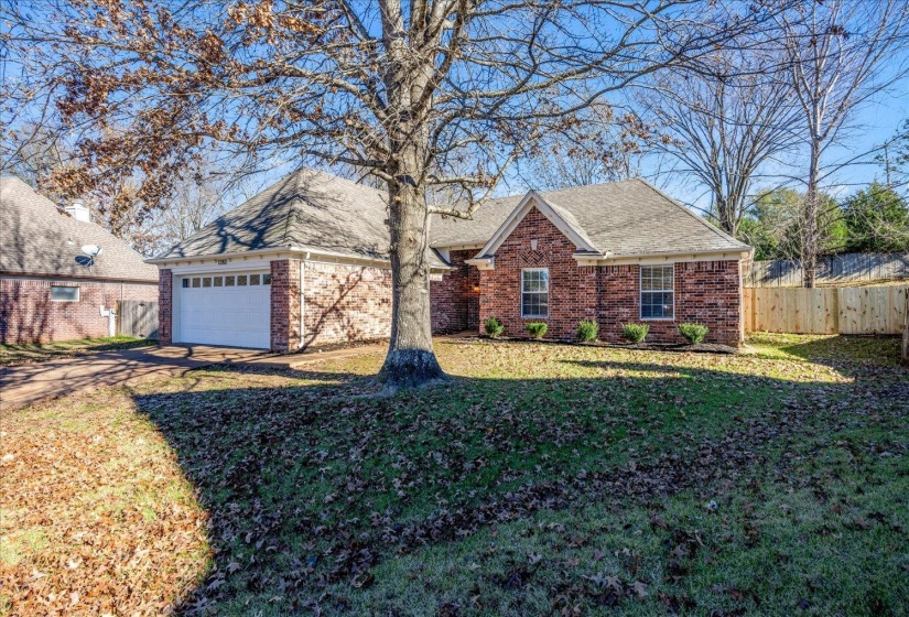 Brick exterior home featuring a two-car garage, pitched shingle roof, and a privacy fence