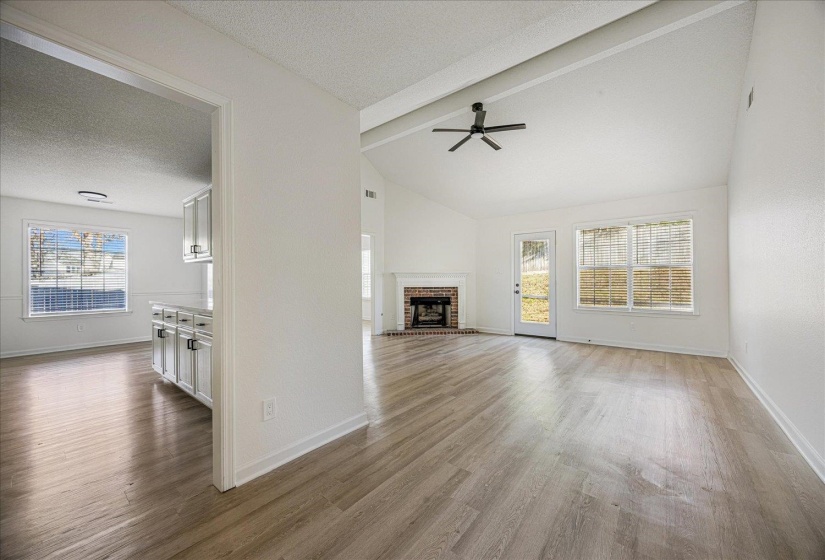 Spacious living area featuring wood-finish flooring, a vaulted ceiling with a ceiling fan, and a brick fireplace
