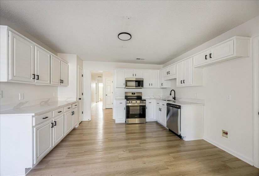 Bright kitchen featuring white cabinetry with black hardware, stainless steel appliances, light-toned countertops, wood-finish flooring, and a black faucet