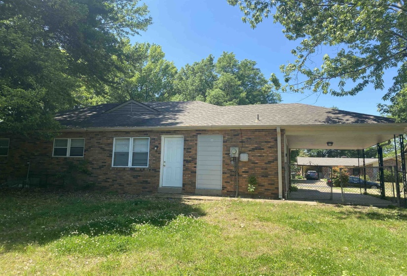 Brick exterior home featuring a covered carport, pitched shingle roof, and white-framed windows