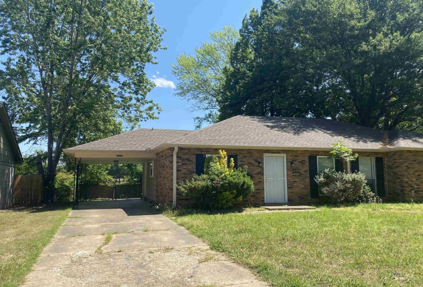 Brick residence featuring a covered carport, pitched shingle roof, and a concrete driveway