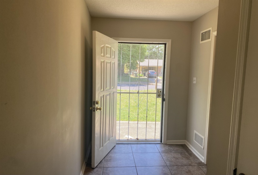 Foyer featuring ceramic tile flooring, neutral wall paint, white trim, and a paneled entry door with security screen