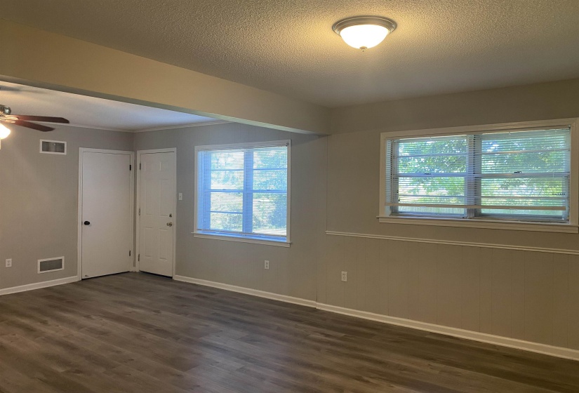 Spacious interior room featuring wood-finish flooring, two windows with blinds, and light neutral wall paint