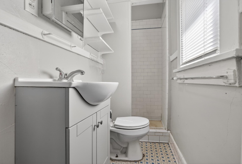 Bathroom featuring a pedestal sink with chrome faucet, a built-in shower with subway tile, patterned floor tiles, and a window with blinds