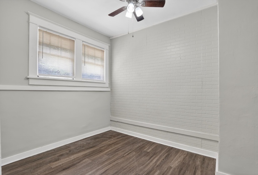 Room featuring wood-finish flooring, white baseboards, and a painted brick accent wall