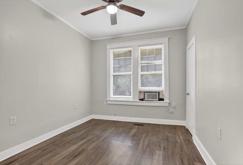 Neutral tone wall color, wood-finish flooring, white trim, ceiling fan, and double windows with a window-mounted air conditioning unit