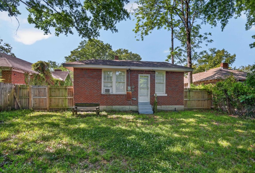 Brick exterior featuring a white entry door, two windows, and a wood privacy fence