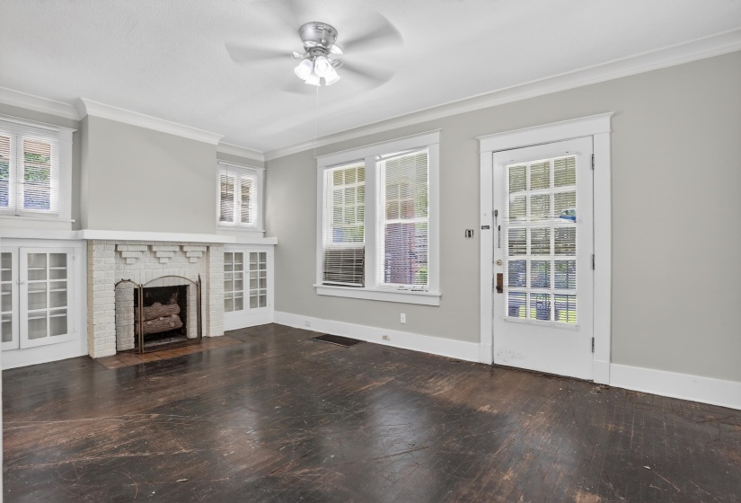 Living space featuring a brick fireplace with white-painted surround, dark wood-finish flooring, and multiple windows