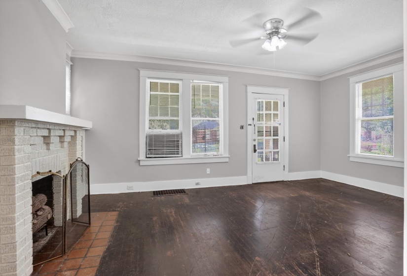 Living area featuring a painted brick fireplace with a tile hearth, dark wood-finish flooring, and crown molding
