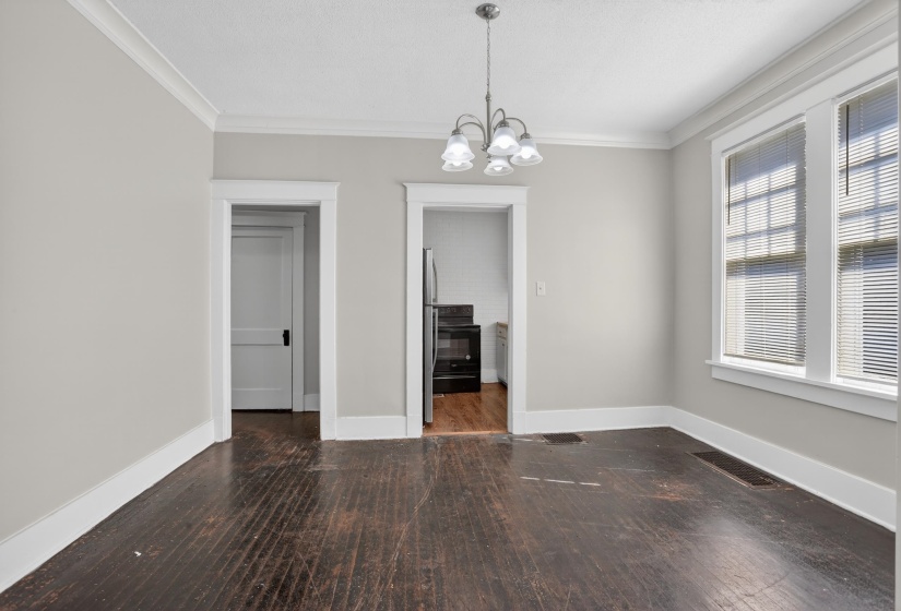Spacious room featuring dark wood-finish flooring, white crown molding, a multi-bulb chandelier, and dual windows with blinds