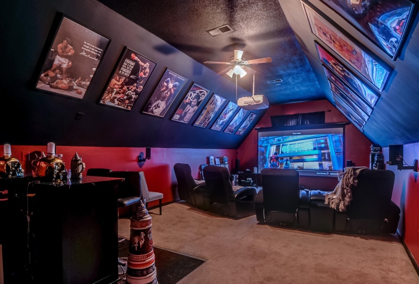 Dedicated media room featuring a large projection screen, recessed projector, and sloped ceiling