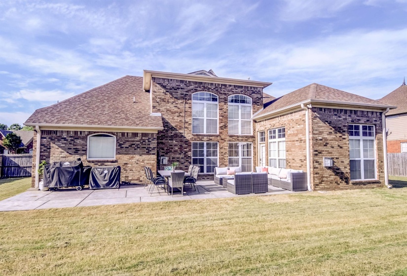 Expansive backyard featuring a concrete patio, brick exterior, multiple large windows, and a shingle roof