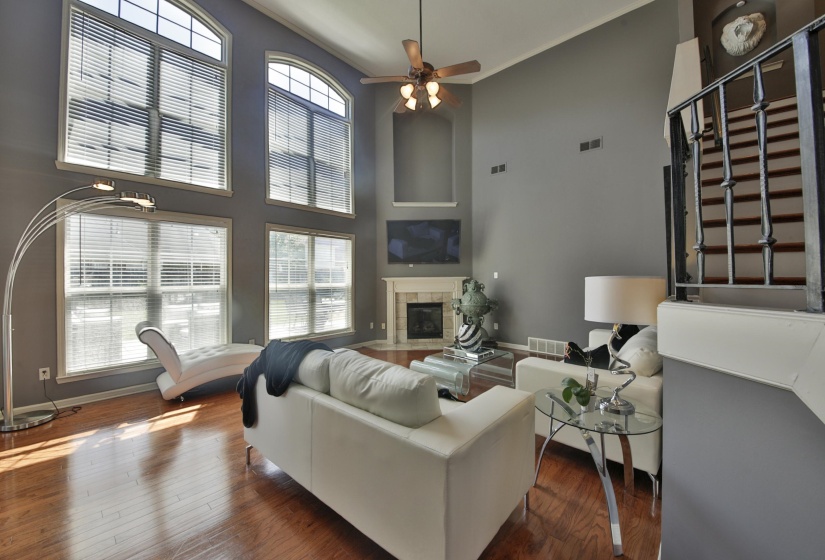 Vaulted living space featuring hardwood flooring, a fireplace with a mantel, and multiple large windows with arch-top elements