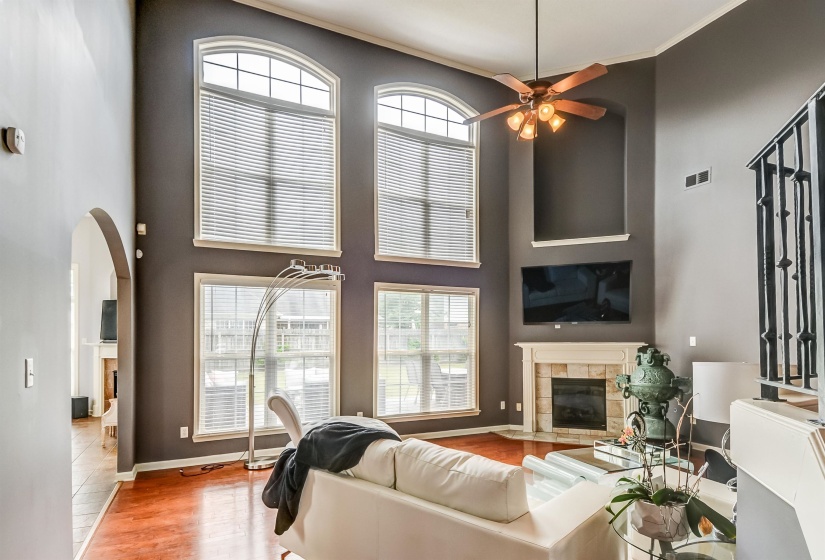 Living area featuring rich wood-finish flooring, high ceilings, and a corner fireplace with a stone surround and mantel