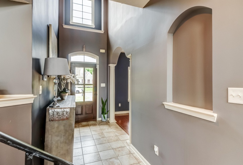 Foyer featuring a tall arched entryway, transom window above the front door, ceramic tile flooring, and decorative wall niche with trim