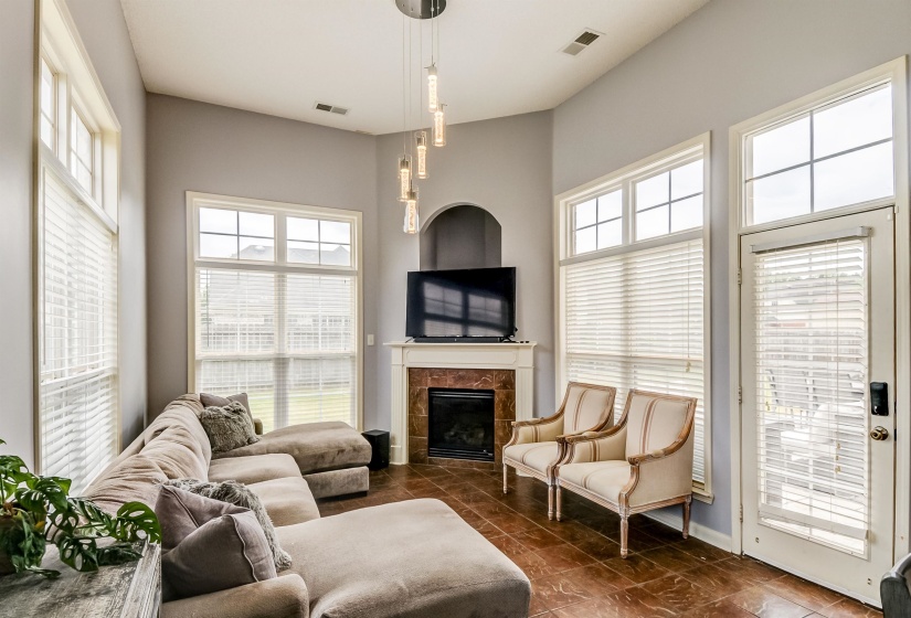 Vaulted ceiling living area featuring a central fireplace with a stone surround and mantel, ample natural light from multiple windows, and a glass-paneled door