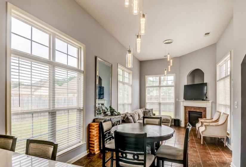 Open-concept living space featuring vaulted ceilings, multiple windows with blinds, a fireplace with a stone surround, an arched alcove, and contemporary pendant lighting