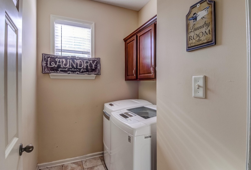 Dedicated laundry area featuring a window, overhead cabinetry, and tile flooring