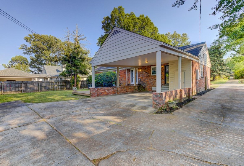 Brick exterior with a covered carport, concrete driveway, and a wood deck
