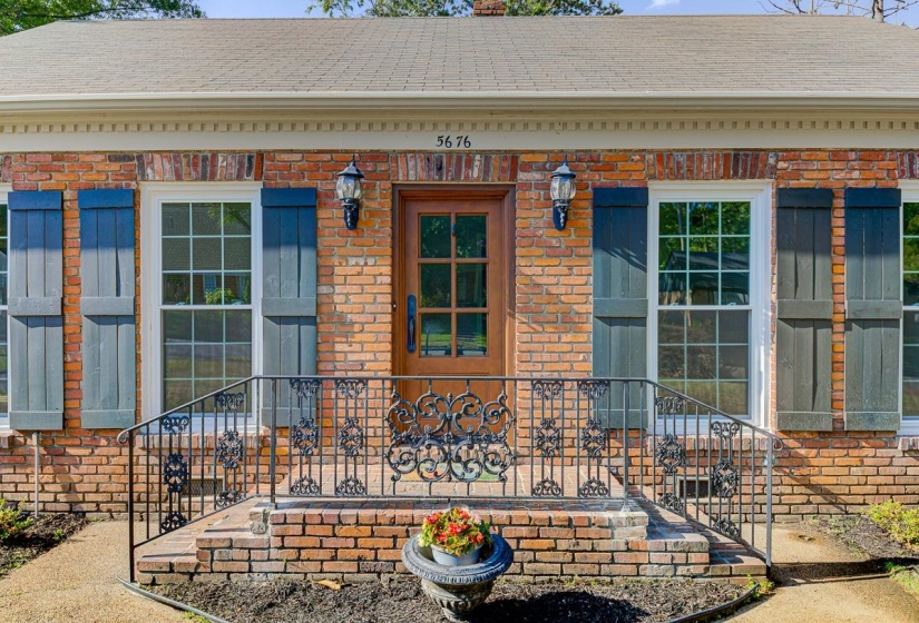Brick exterior with a wooden entry door, flanked by shuttered windows