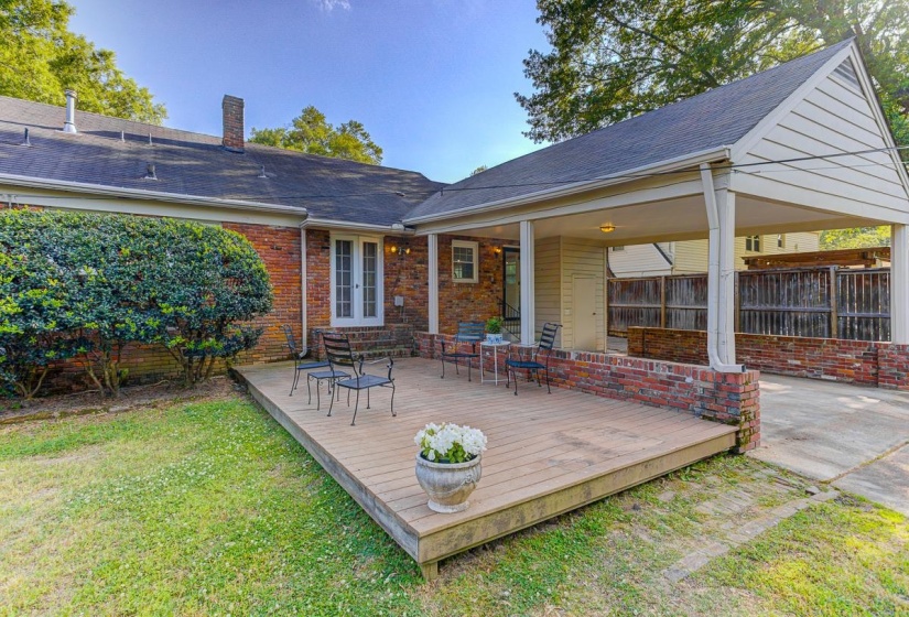 Rear exterior featuring an elevated wood deck, brick facade, a covered carport, and a mature shrub