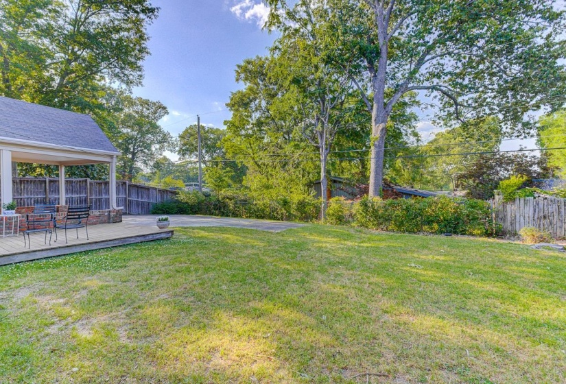 Expansive backyard featuring a large grass area and a covered wood deck
