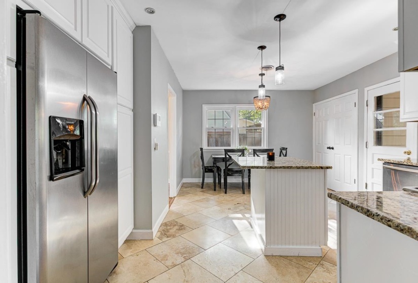 Stainless steel side-by-side refrigerator, white upper cabinetry, light-toned tiled flooring, a kitchen island with beadboard paneling and a granite countertop, and pendant lighting fixtures