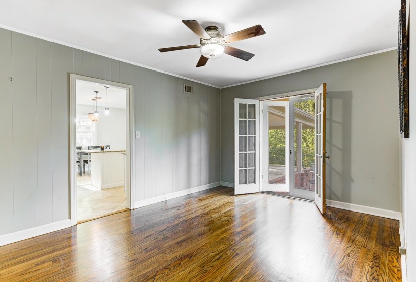 Interior room featuring rich wood-finish flooring, light grey wall paneling, and a ceiling fan with integrated lighting