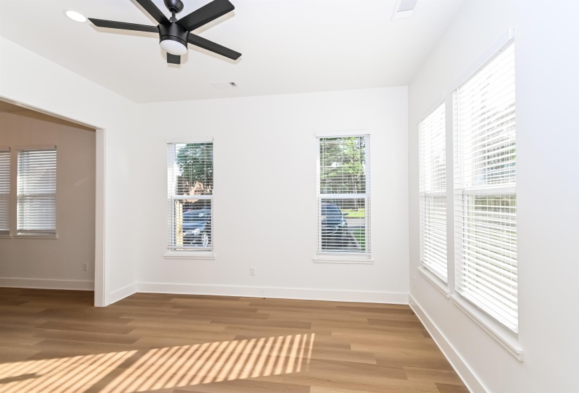 Spacious interior featuring a modern ceiling fan, multiple windows with blinds, light wood-finish flooring, and white walls