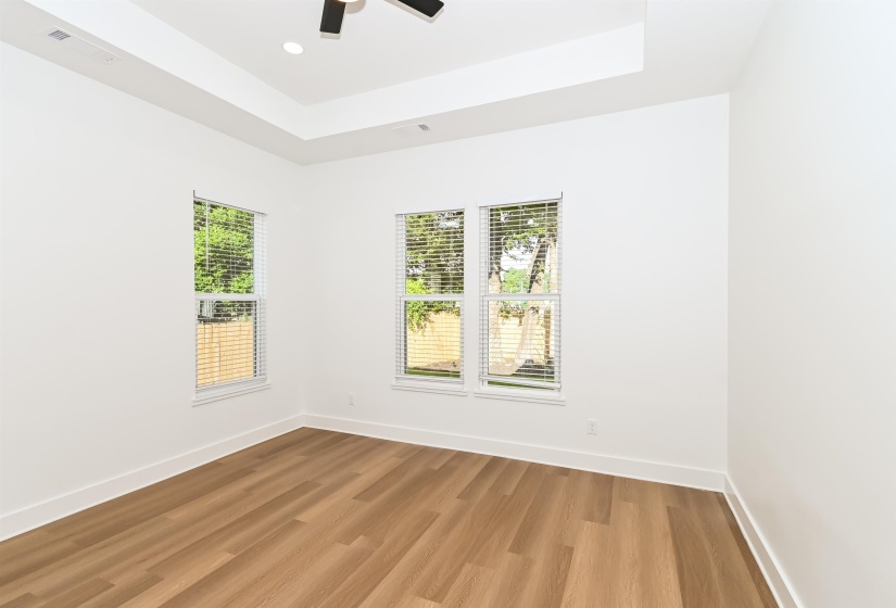 Spacious interior room featuring a tray ceiling with recessed lighting, wood-finish flooring, and multiple windows with blinds