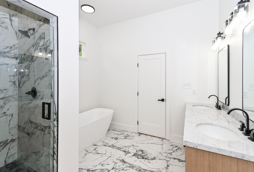 Bathroom featuring a glass-enclosed shower with black fixtures, a freestanding soaking tub, dual vanity with undermount sinks, and marble-look flooring