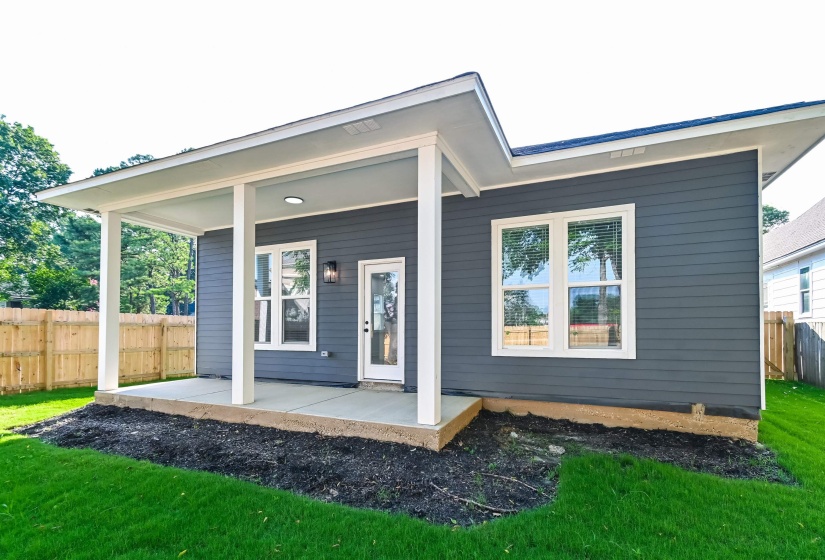 Rear exterior featuring a covered concrete patio, dark gray horizontal siding, and a wooden privacy fence