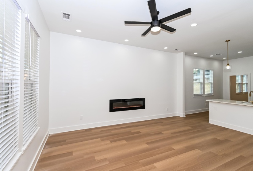 Open-concept living area featuring wood-finish flooring, a contemporary linear fireplace, and recessed ceiling lighting