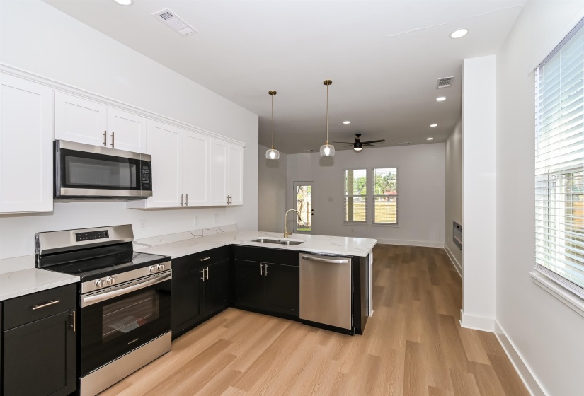 Open-concept kitchen featuring two-tone cabinetry with stainless steel appliances, a stainless steel sink with a gooseneck faucet, quartz countertops, and wood-finish flooring