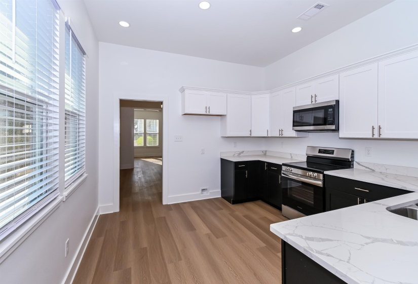 Contemporary kitchen featuring wood-finish flooring, two-tone cabinetry with white upper and black lower cabinets, stone-finish countertops, and recessed lighting