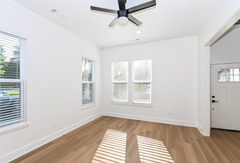 Spacious interior room featuring wood-finish flooring, a contemporary ceiling fan, multiple windows with blinds, recessed lighting, and a white paneled door with glass inserts