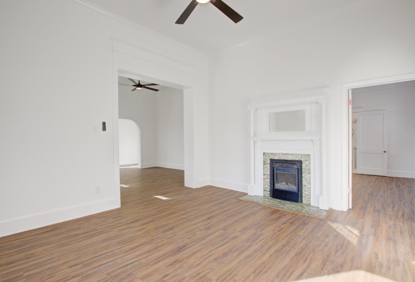 Unfurnished living room with wood finished floors, ceiling fan, arched walkways, and a fireplace with flush hearth
