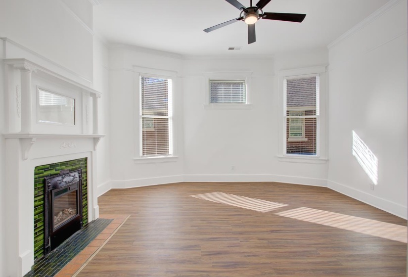 Unfurnished living room featuring wood finished floors, a fireplace, ceiling fan, and crown molding