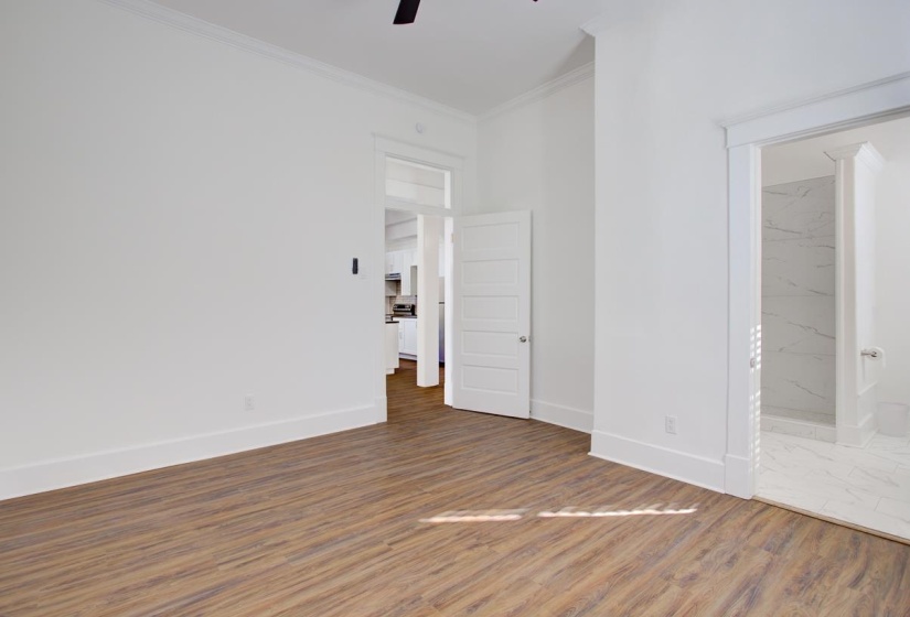 Unfurnished bedroom with ornamental molding, wood finished floors, ensuite bathroom, and ceiling fan