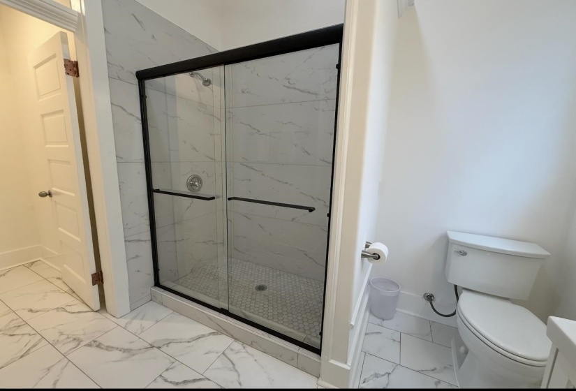 Full bath featuring light marble finish floors and a marble finish shower