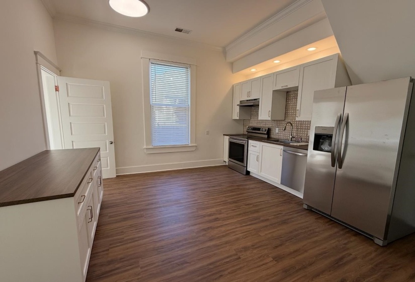 Kitchen with dark countertops, stainless steel appliances, ornamental molding, dark wood finished floors, and backsplash