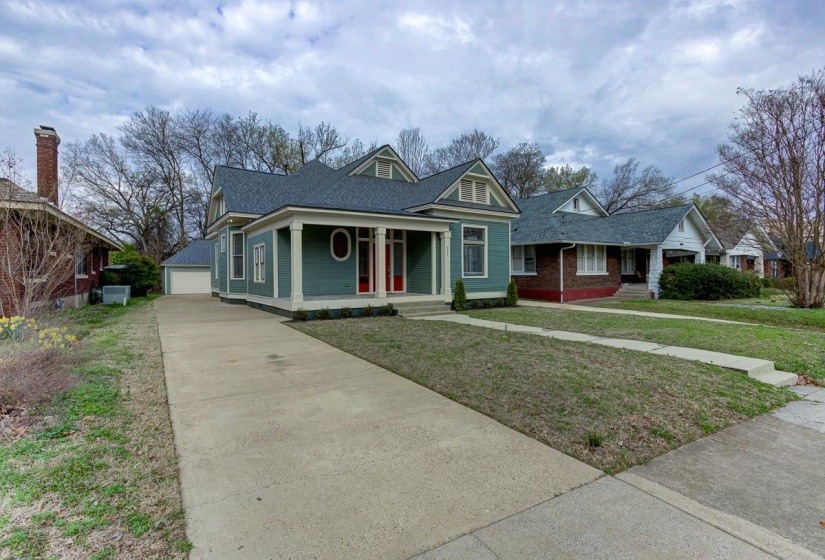 View of front of home featuring a porch, a detached garage, an outdoor structure, a front lawn, and a shingled roof