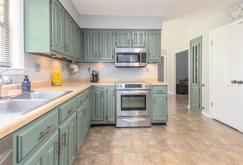 Kitchen with green cabinetry, stainless steel appliances, light countertops, and stone finish flooring