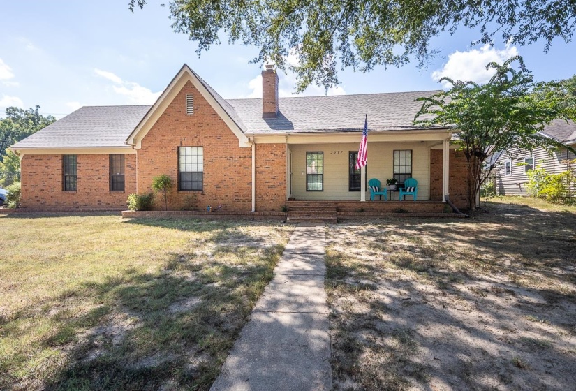 Ranch-style house featuring covered porch, brick siding, a chimney, a shingled roof, and a front yard