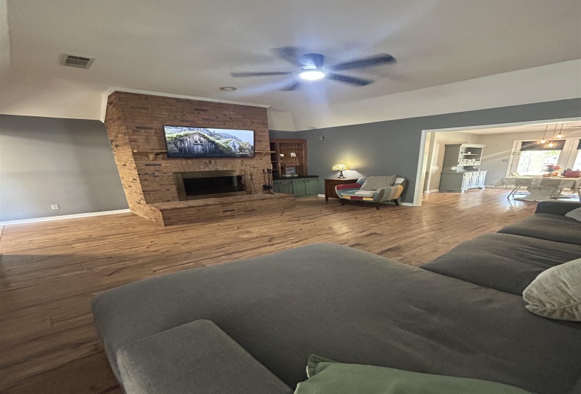 Living room with wood finished floors, a ceiling fan, and a brick fireplace